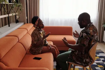 A couple sitting on different seats in their living room, having a stern conversation